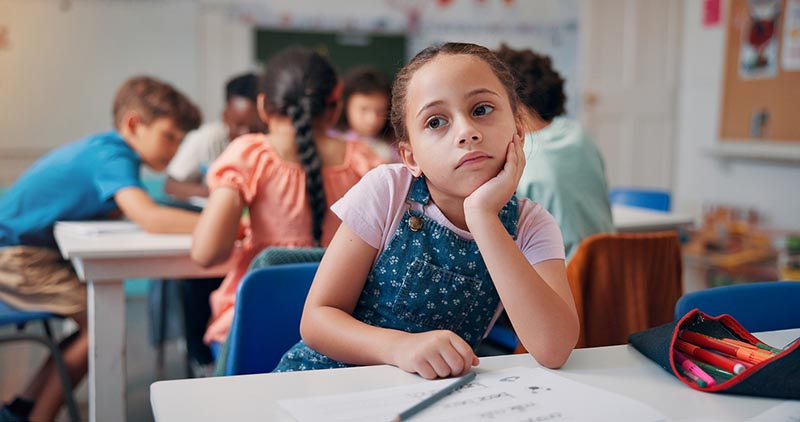 Child in classroom showing ADHD-related inattention by resting bored face in hand