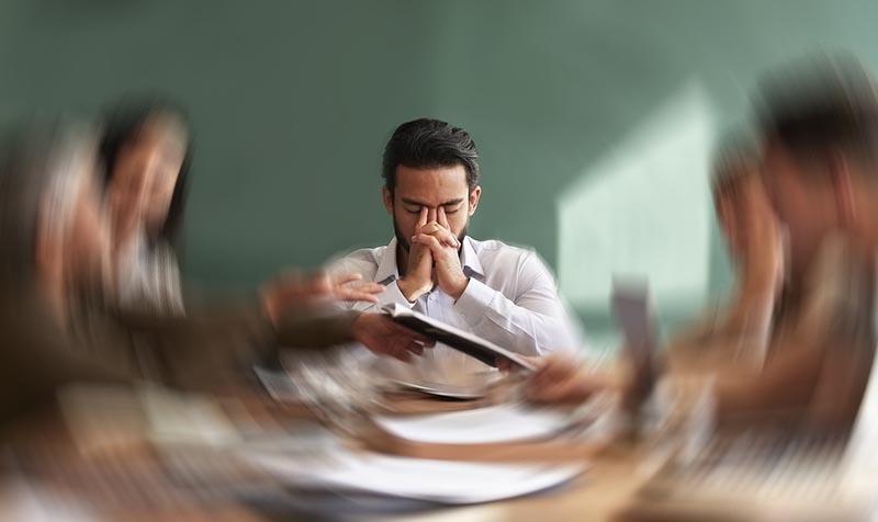 Man overwhelmed in crowded room, hands clasped over face illustrating anxiety symptoms