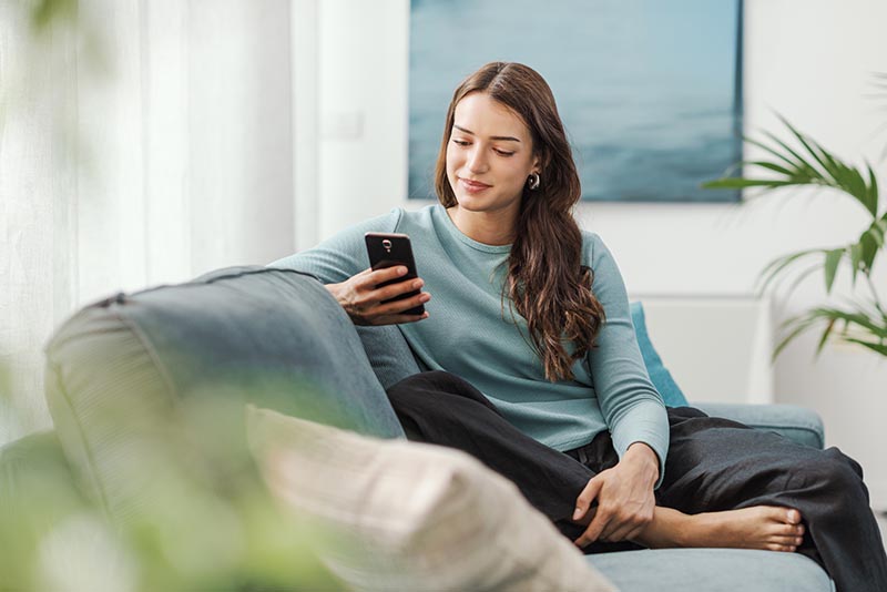 Woman relaxing on couch checking phone, ready to reach out for counseling support